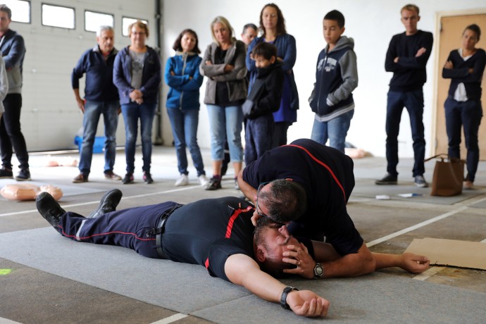 Simulation. « Monsieur, vous m’entendez ? Serrez-moi la main, ouvrez les yeux ! » Les pompiers montrent aux participants la conduite à tenir face à une victime inconsciente. Ici, le sauveteur maintient la tête et vérifie la respiration.